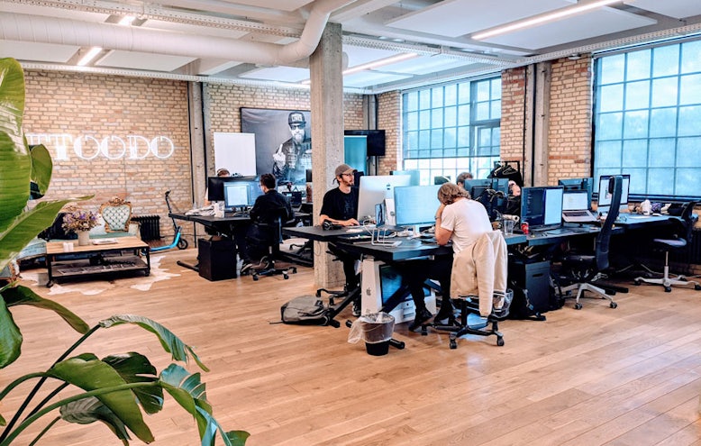 The open-plan office with brick walls, tall factory windows and a lounge corner